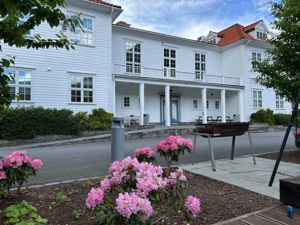 Kvitt trebygg med rosa blomar i framgrunnen.